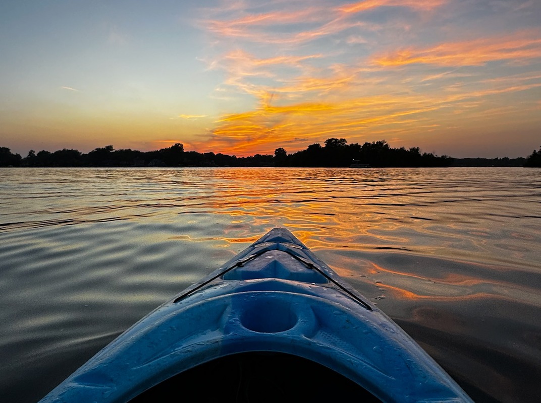 Bow of a blue kayak on a lake at sunset