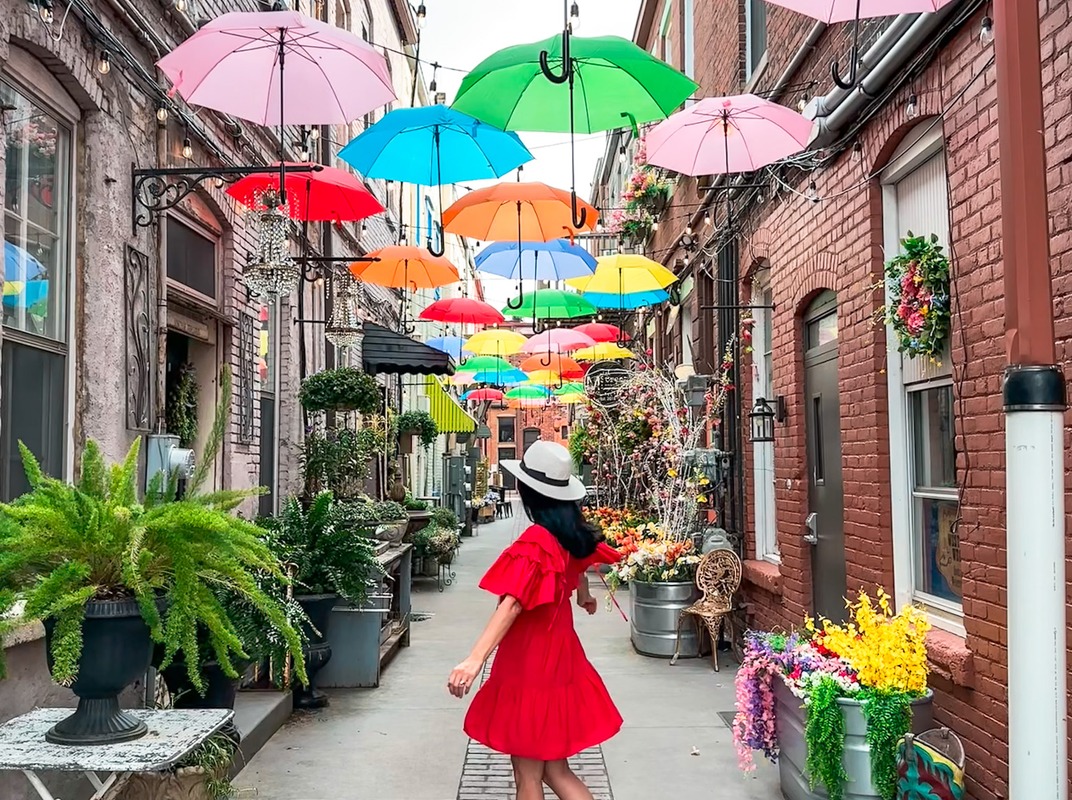 Heather in a red dress under an alley of colorful umbrellas